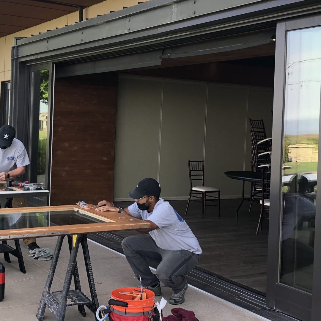 Two men working on a table outside of an open patio.